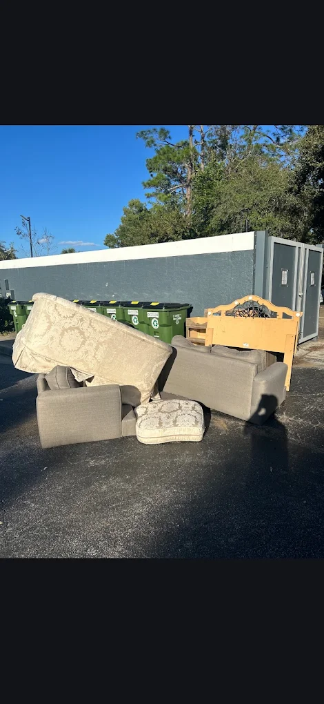 Before photo of a couch, headboard, and cushions dumped by an apartment dumpster enclosure